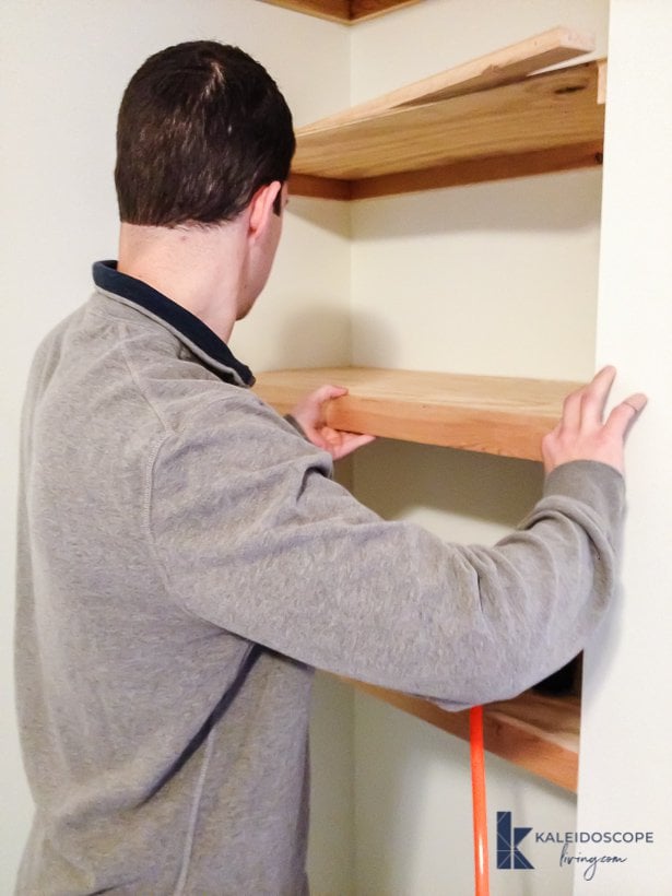 man installing DIY floating shelves in corner of bedroom