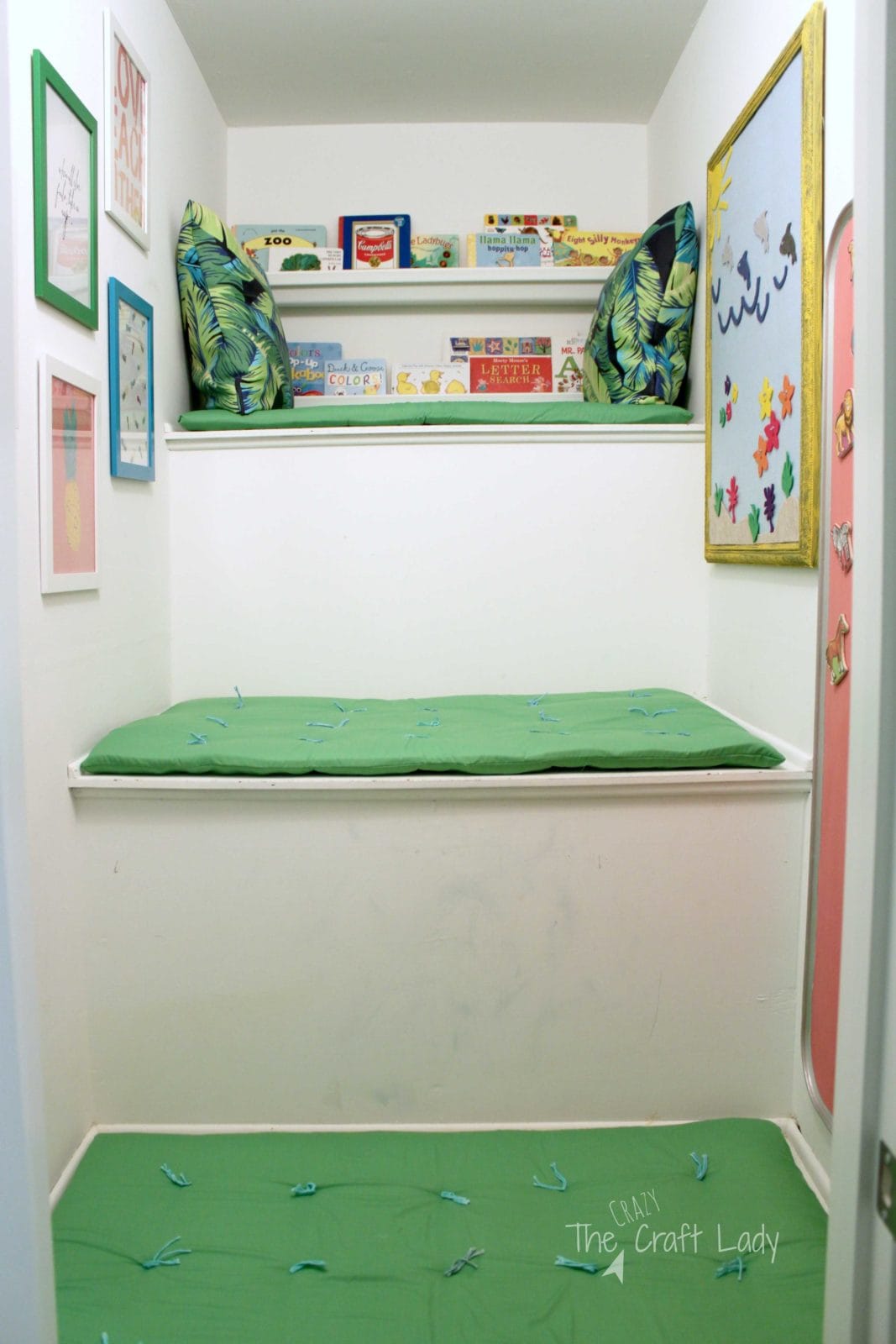 A transformed odd-shaped storage closet is now a play space for kids, complete with green cushions on a bench, children's artwork on the wall, books and pillows on the upper shelves and seating to relax. 