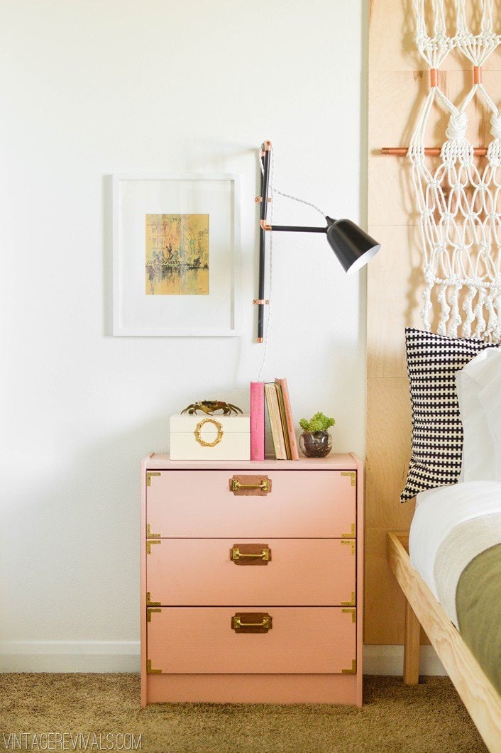 A Campaign dresser hack from an IKEA Rast is featured next to a bed. The dresser has three drawers with brass details.