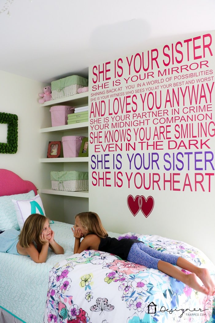 little girls laying on bed with sister quote on wall behind them