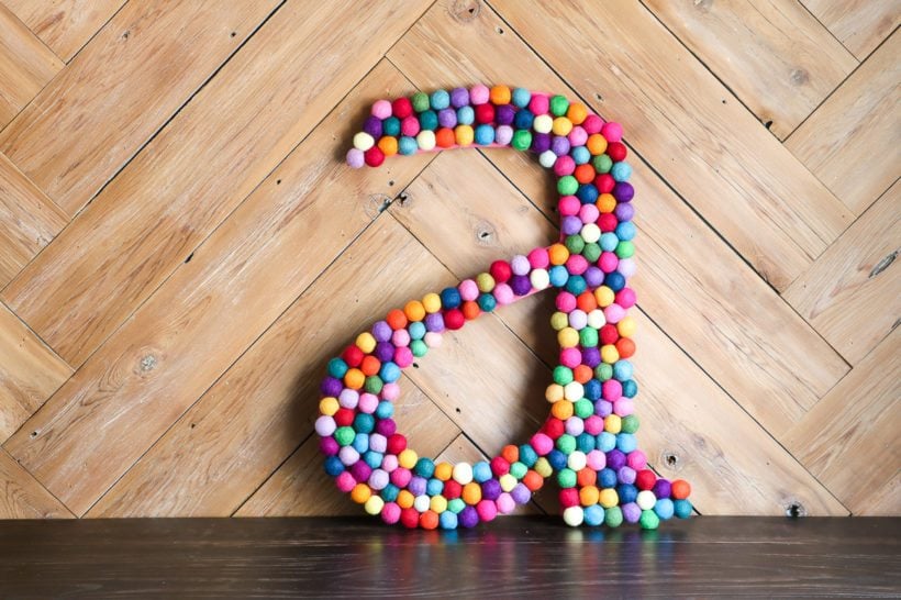 large DIY rainbow felt ball letter leaning on wood wall