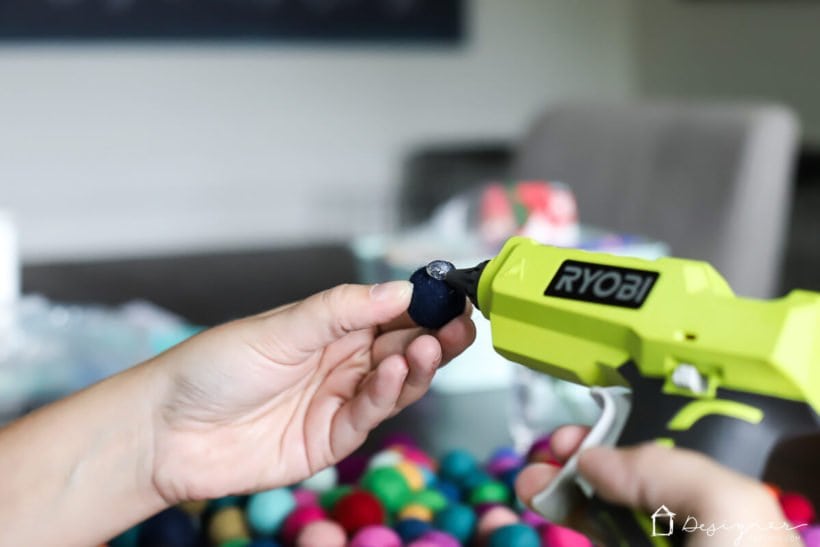 photo of woman using hot glue gun to glue colorful felt balls onto styrofoam wreath form