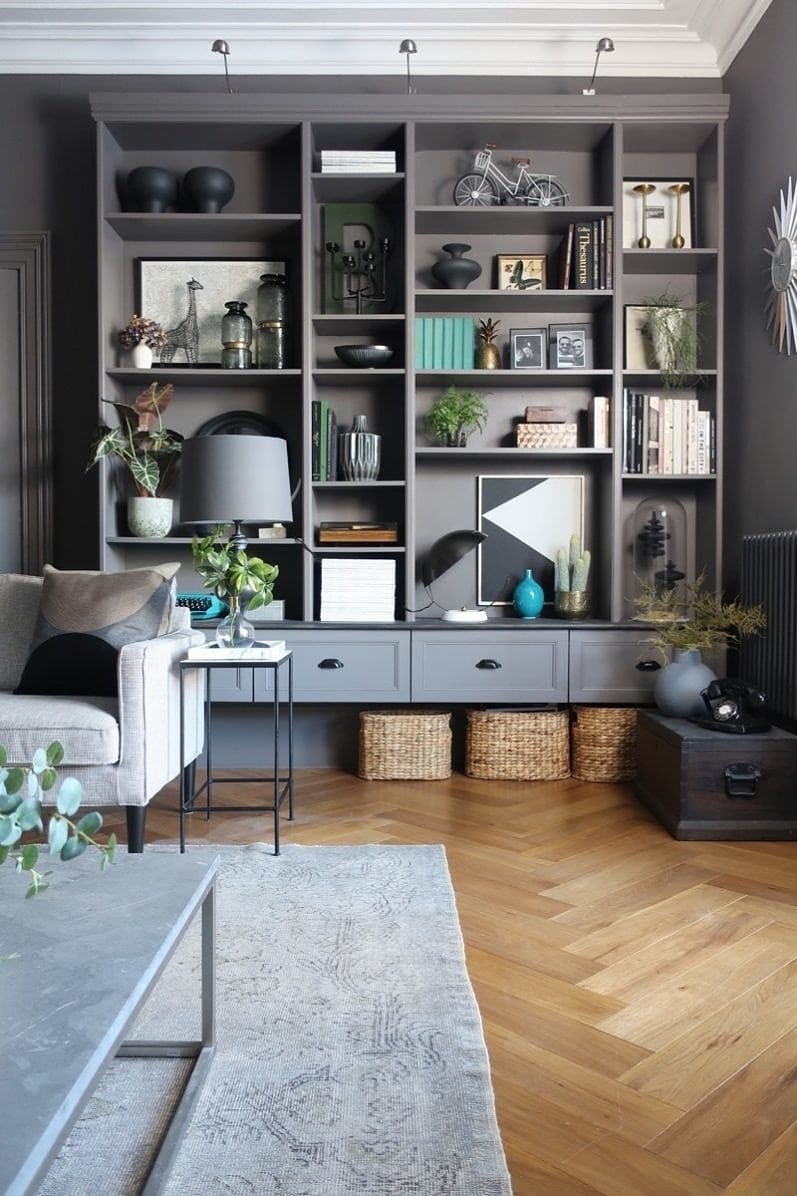 Various sizes of shelves made from  bookcases are along the back wall of a living room. The shelves are full of plants, books and knickknacks thanks to a DIY IKEA hack. 