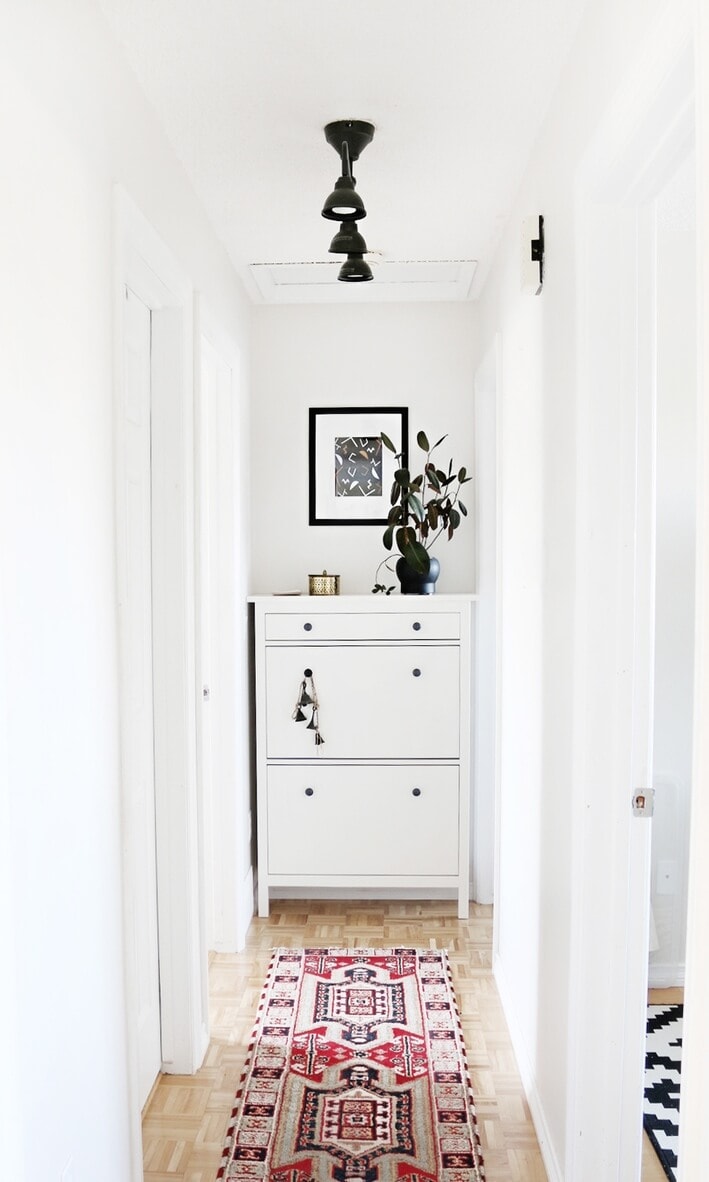 white hallway with dresser at end and bright rug