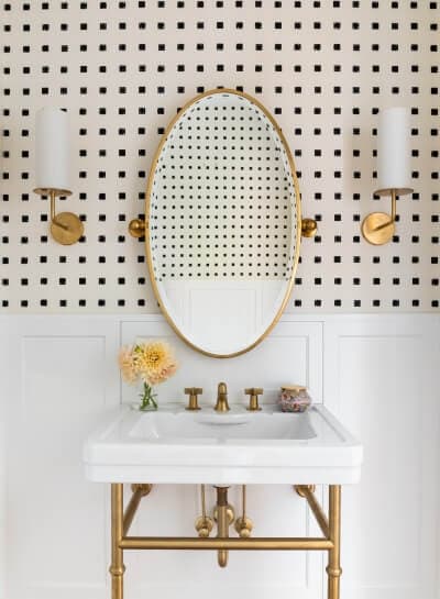 bathroom with white porcelain sink with gold legs and pipes, gold mirror and black and white wallpaper