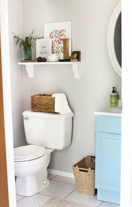 light blue vanity with white walls and small shelf above the toilet