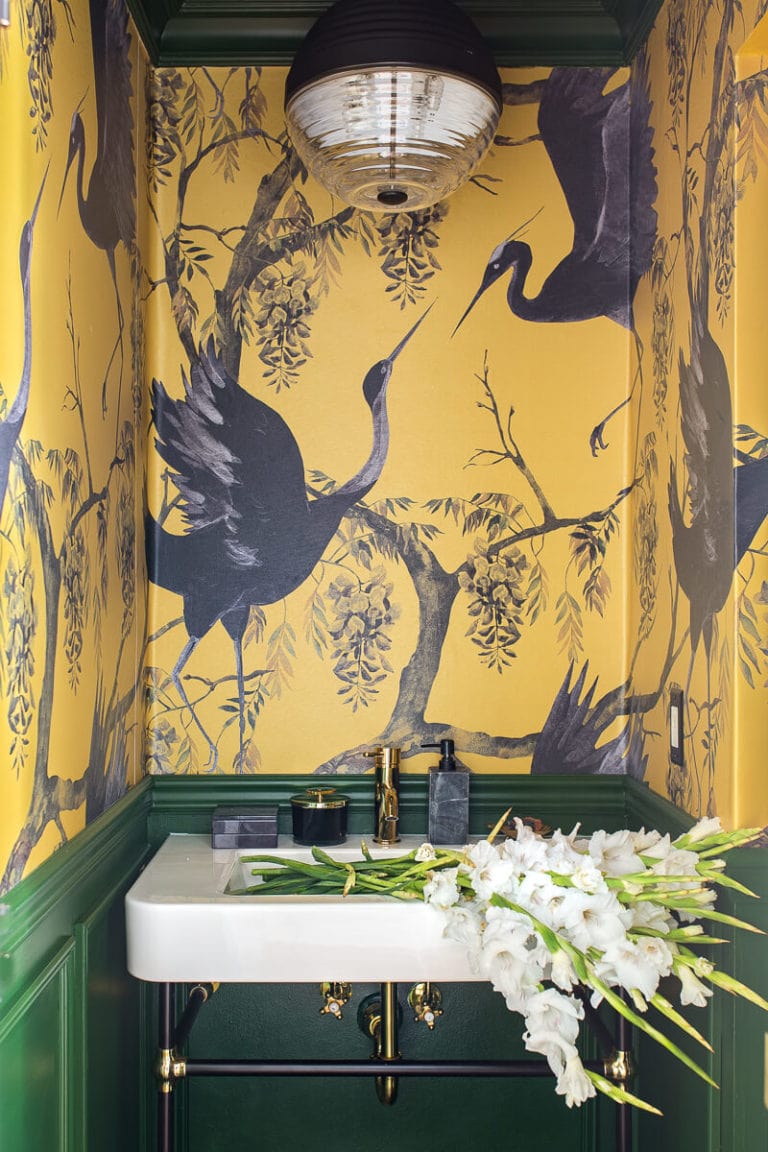 mustard wallpaper with cranes and emerald green walls below with sink filled with flowers