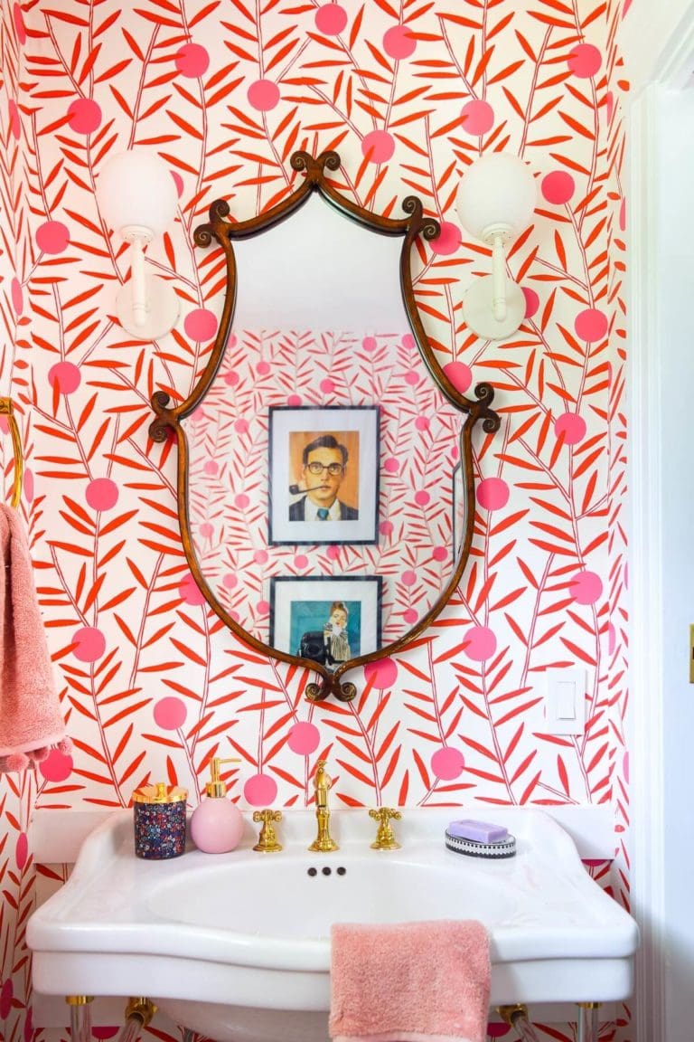 bold pink and red wallpaper with pictures reflected in mirror over sink