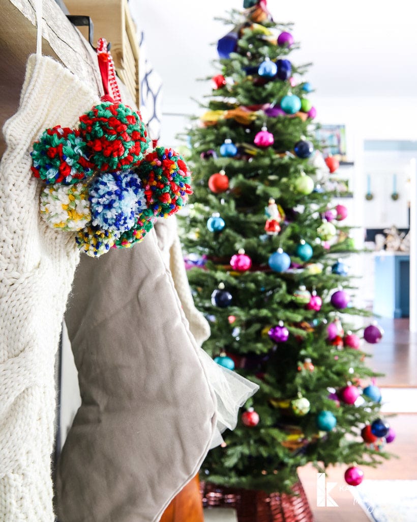 pom pom stocking with colorful Christmas tree in background