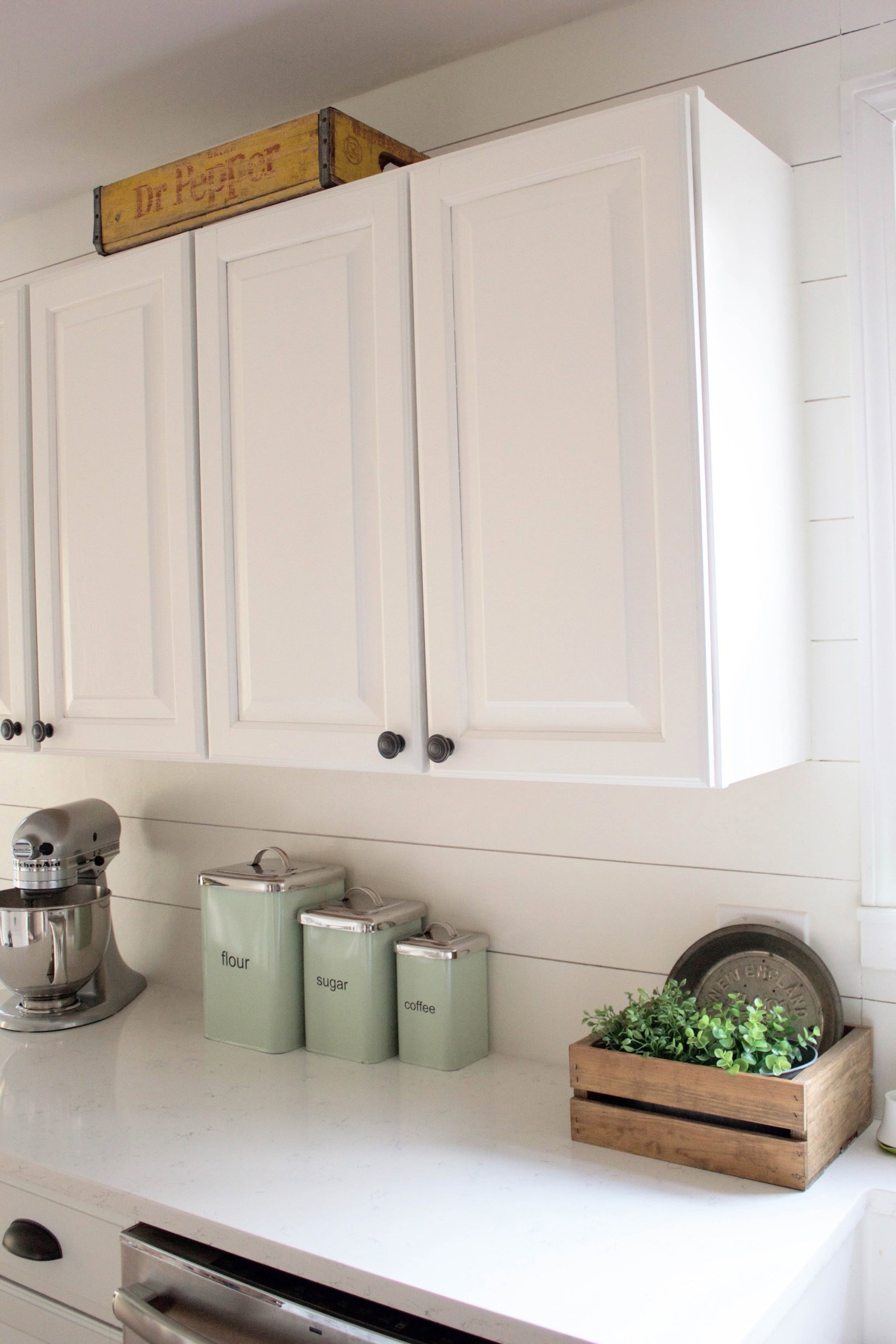 A close-up of a farmhouse kitchen counter, featuring DIY painted kitchen cabinets using Benjamin Moore Advance Paint, and mint green "flour," "sugar," and "coffee" tins.