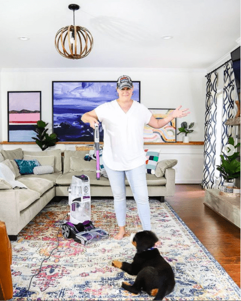 woman cleaning rug with Hoover carpet cleaner while dog watches