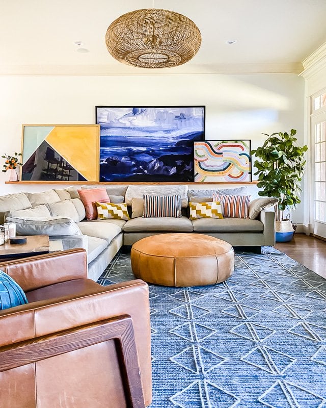 Large living room with sectional and large colorful art on a picture ledge.