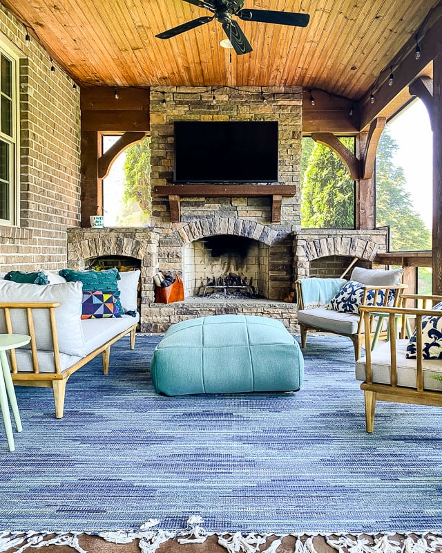 An indoor-outdoor rug on screened in porch in front of a brick fireplace.