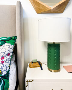 A wooden block serves as one of many personal and family charging stations. The wireless charging station sits on a nightstand next to a green lamp and a white bed.