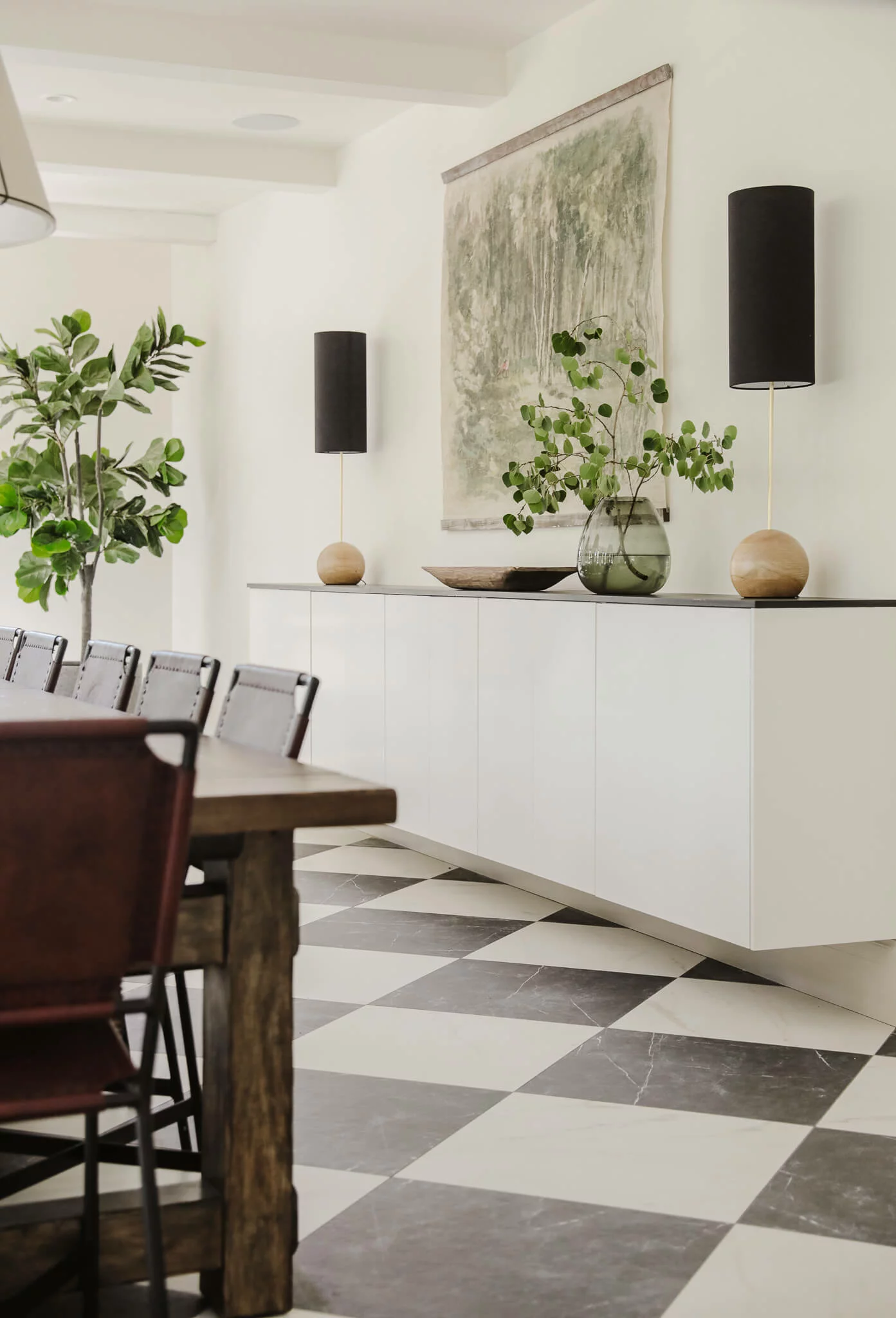 A stark dining room has used upper IKEA kitchen cabinets as a floating buffet and decorative shelf. A dark dining room table and deep green plants add to the beauty of this minimal room.  