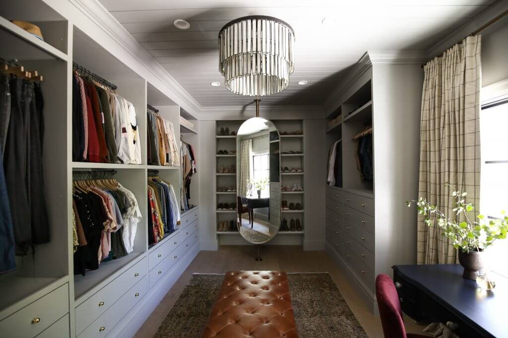 A large closet the size of a small room is lined with built-ins made from IKEA Pax shelves and drawers.  Clothes hang from every open shelf. 