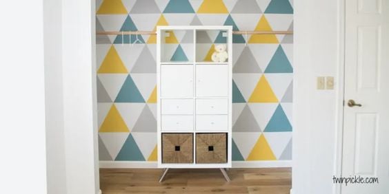 A graphic wall with triangle patterns has a IKEA Kallax unit in front to provide additional storage. 