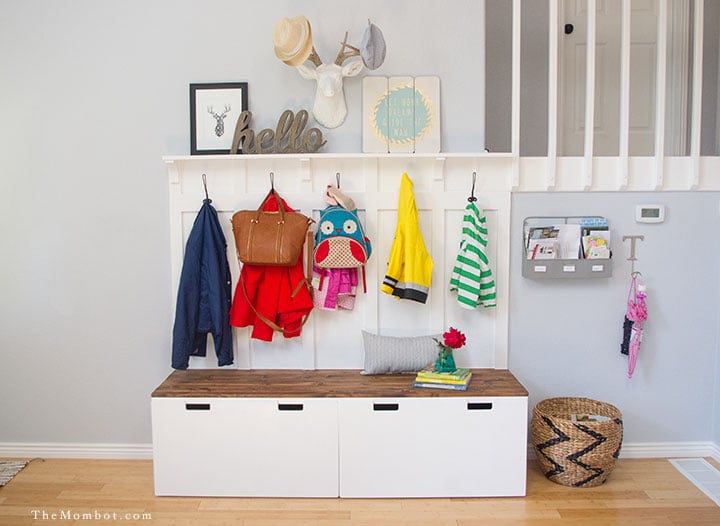 A mini-mudroom for children includes an IKEA Stuvas unit, lower hooks with coats and bags hung above a bench with large square storage bins underneath.