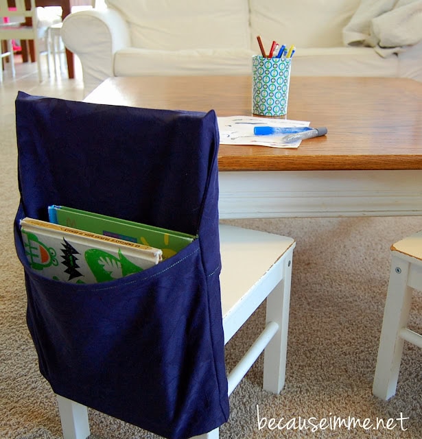 A blue handmade schoolbook organizer hangs from the back of a white chair in front of a table.