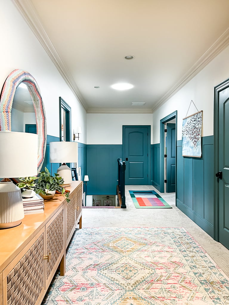 A large home's hallway with blue accent walls and a light, decorative area rug. 