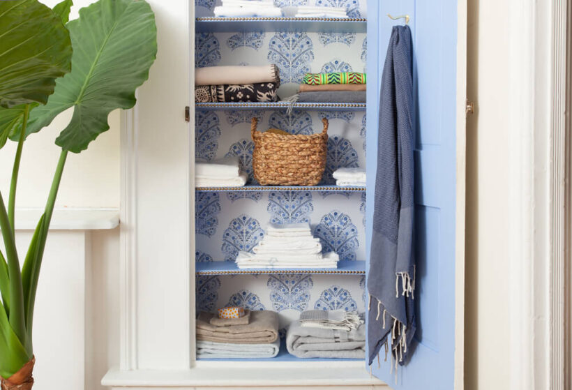 bathroom linen closet with wallpaper and nailhead trim on shelves