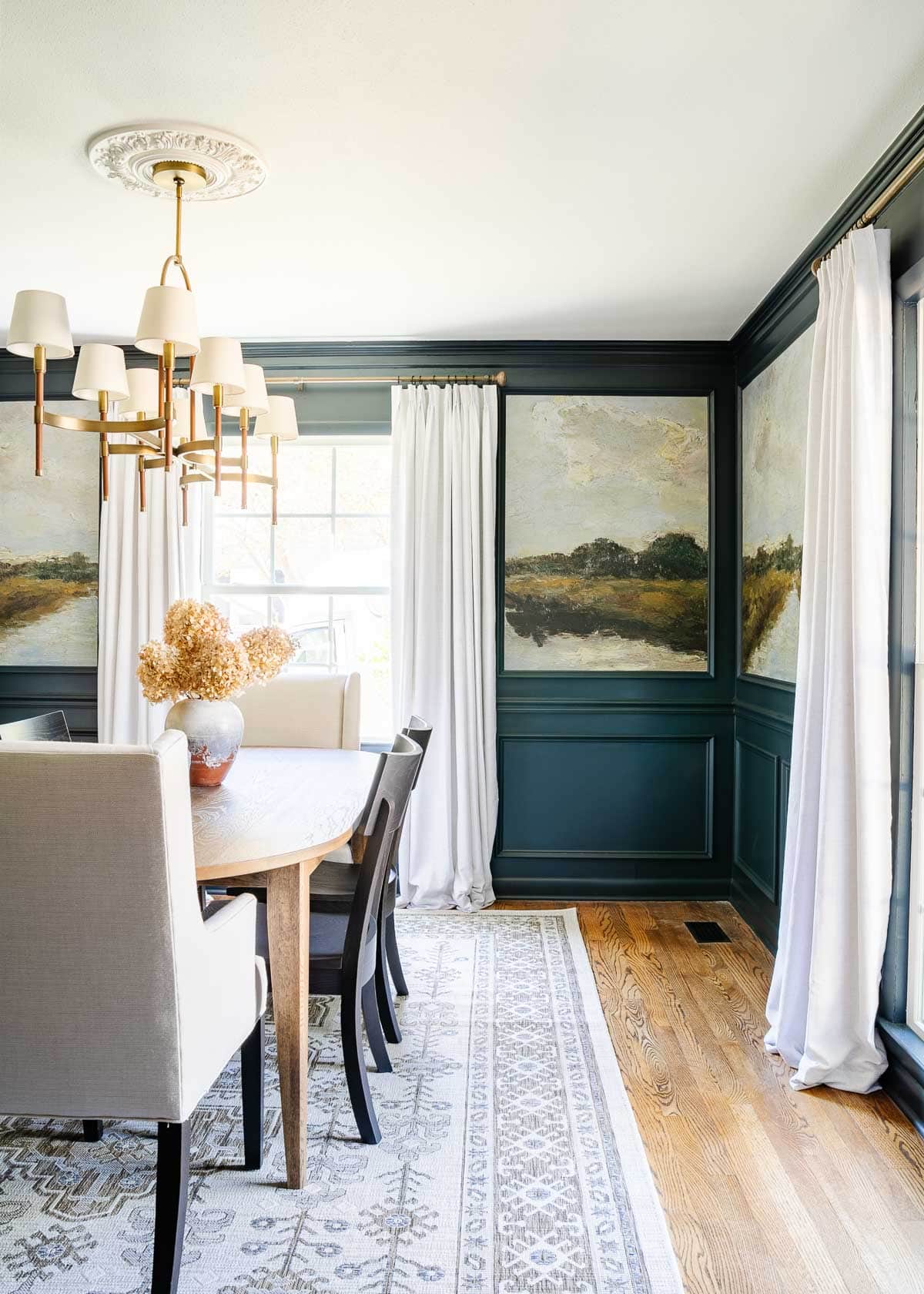 Navy dining room walls with a landscape wallpaper in the middle, a dining room table and area rug. 