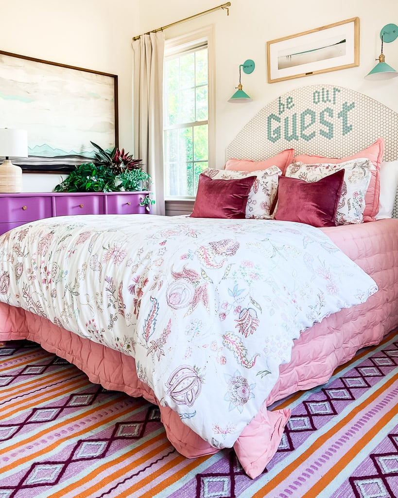 An 8 x 10 pink, purple, and orange area rug under a queen size bed in a colorful guest room.