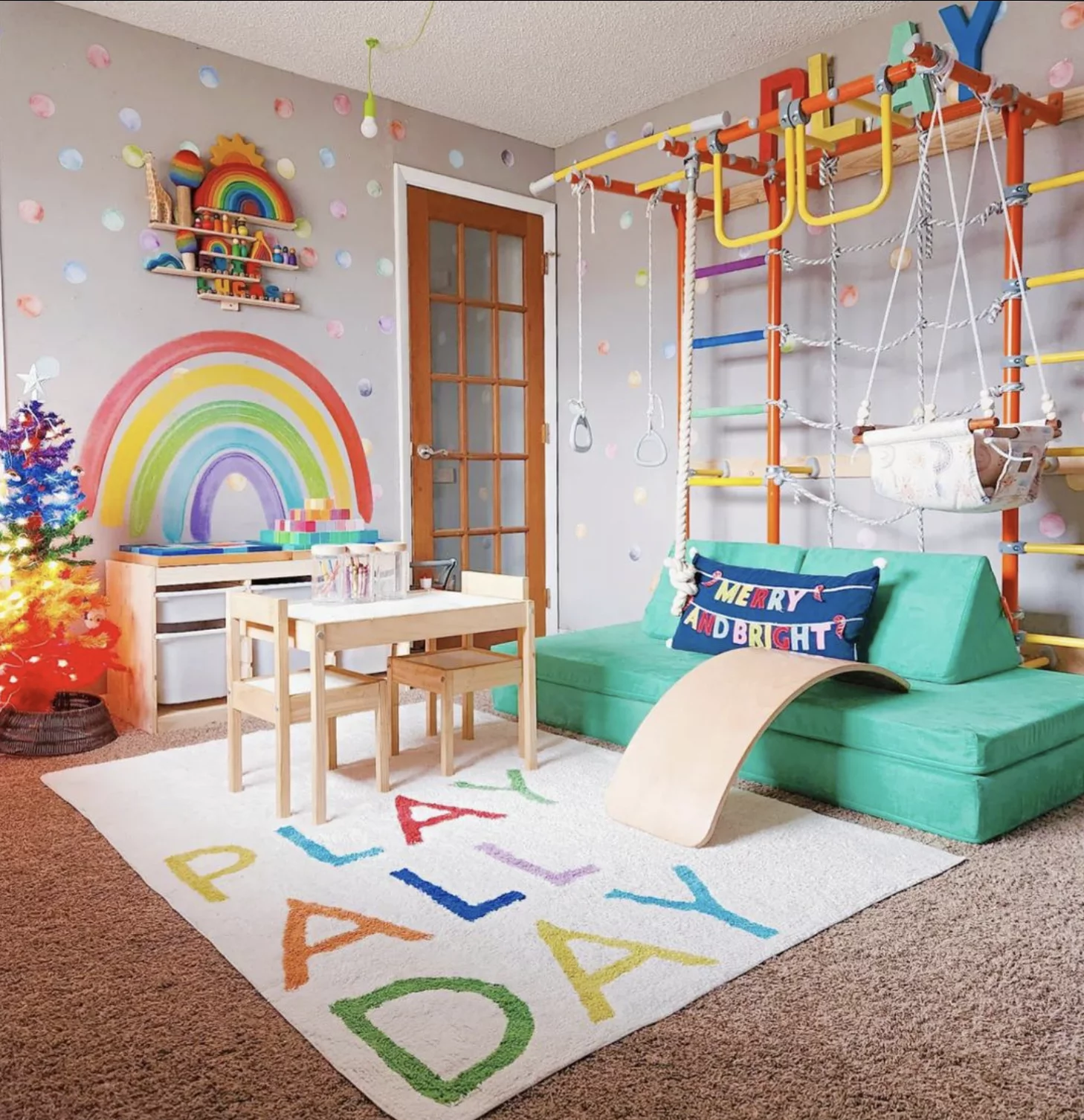 A colorful indoor gym and playroom for young children includes a play table, storage bins, and a green couch. The rug says "Play all day."