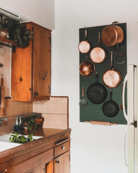 dark green peg board with cooper and cast iron pots and pans