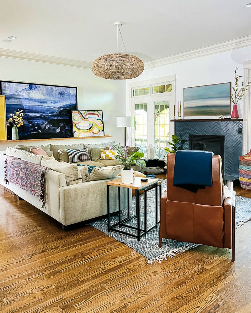 colorful living room with tan sofa, large art on ledge, and blue and white rug on floor