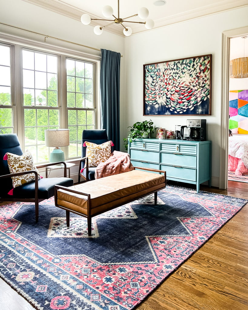 A colorful sitting room with floor to ceiling windows with a coffee station and a graphic West Elm area rug. 