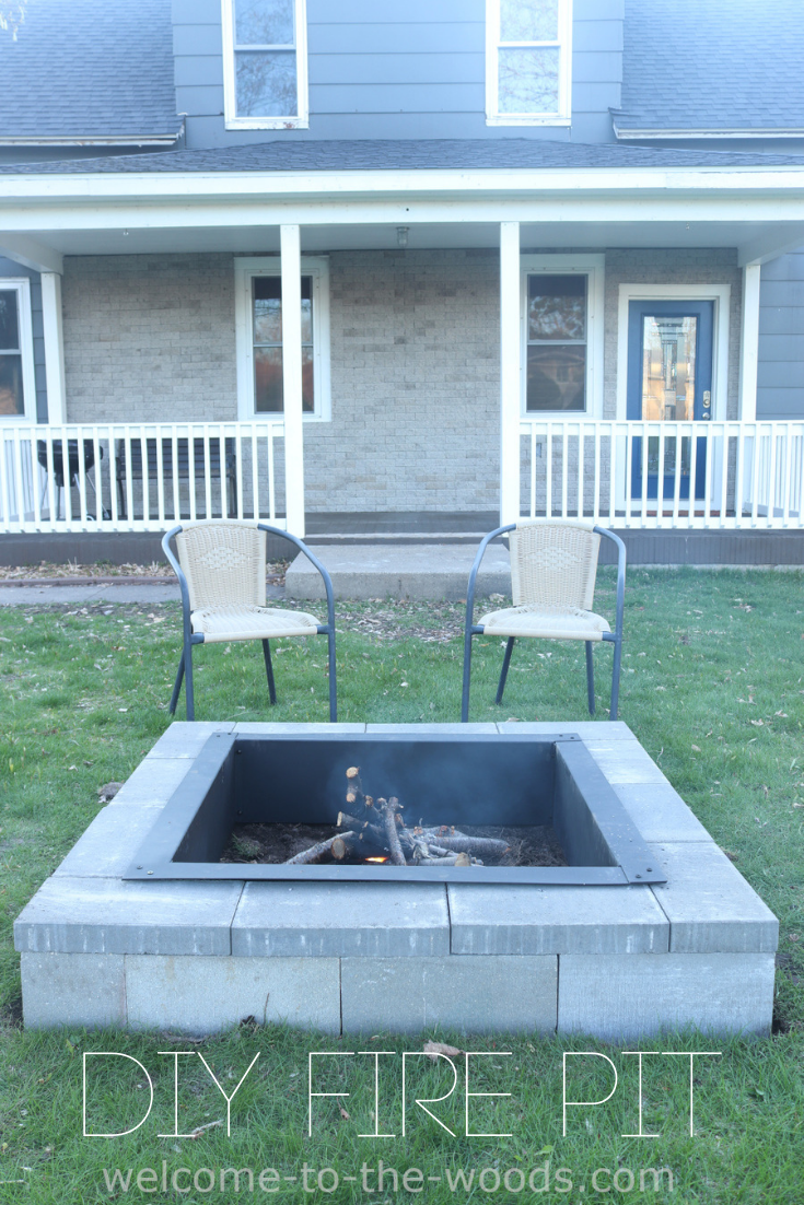 A square fire pit sits in the center of a backyard with square pavers leading from the white porch to the fire pit.