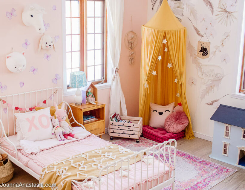 feminine little girls room with white iron toddler bed and reading nook with canopy