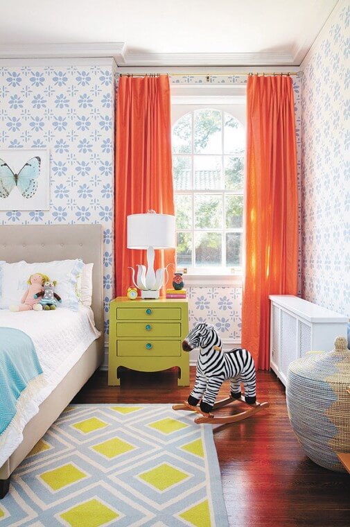 bedroom with periwinkle block print flowered wallpaper, bright orange curtains and pops of teal and chartreuse