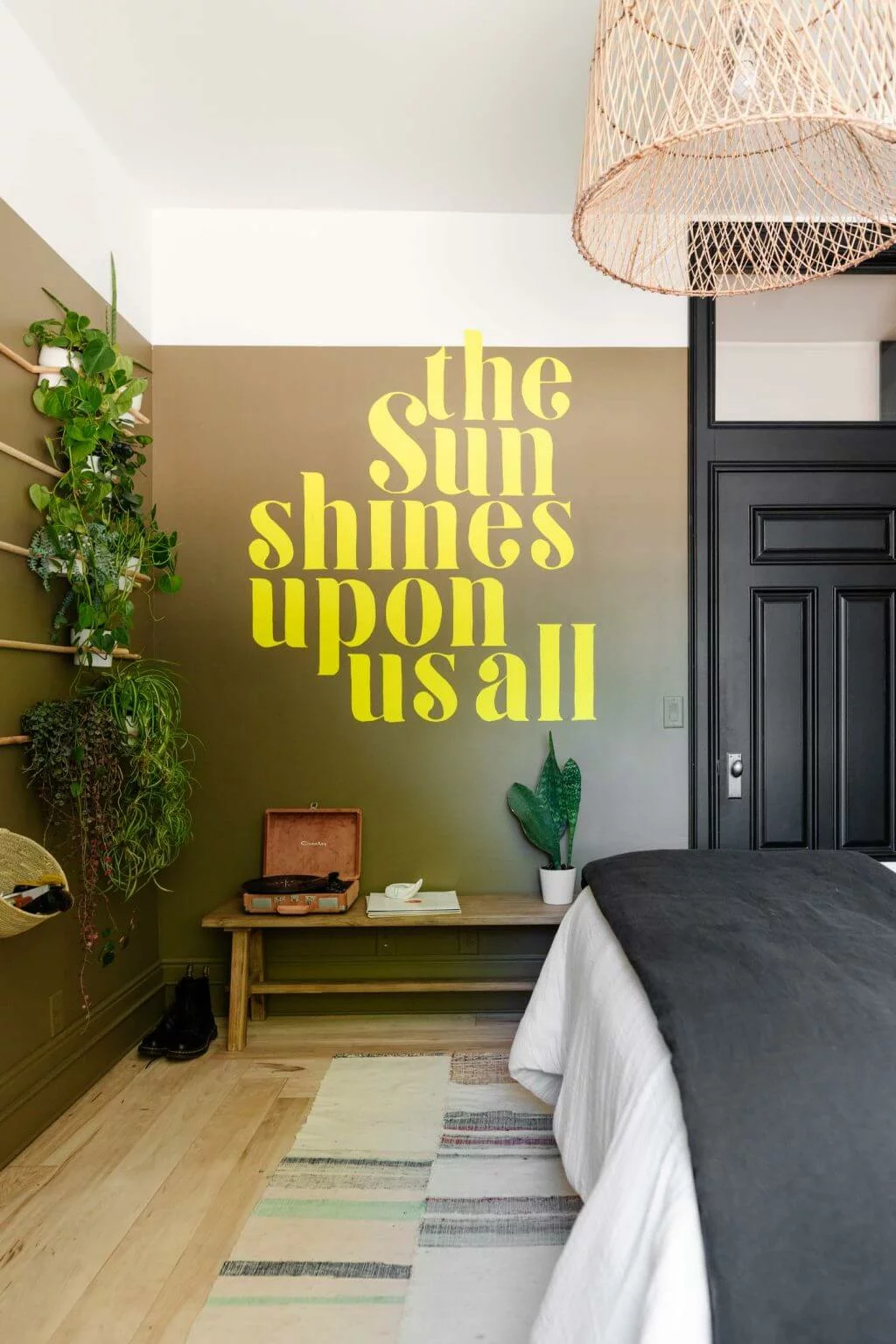 A teen girl's bedroom with a wall of plants, and "the sun shines upon us all" painted on the wall in large yellow letters. 