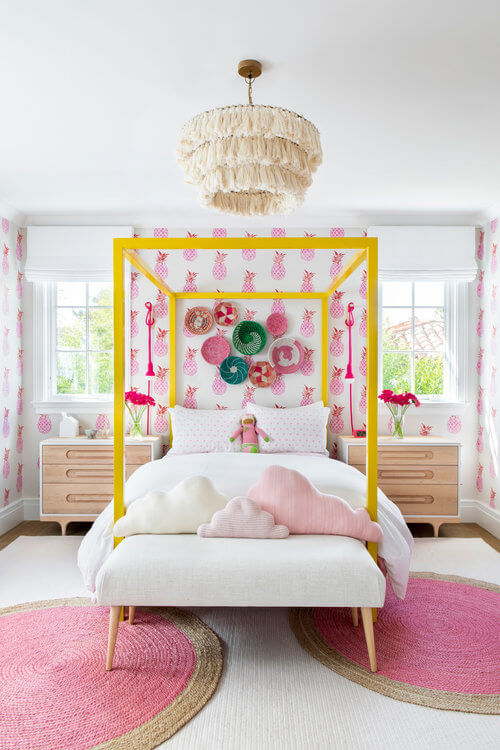 girls bedroom with pink pineapple wallpaper and yellow four poster bed with white bedding.