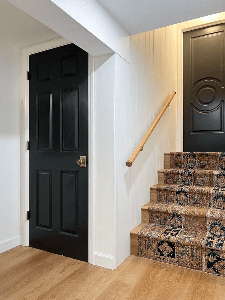 rounded white oak handrail with aged brass end caps and brackets in short basement stairwell