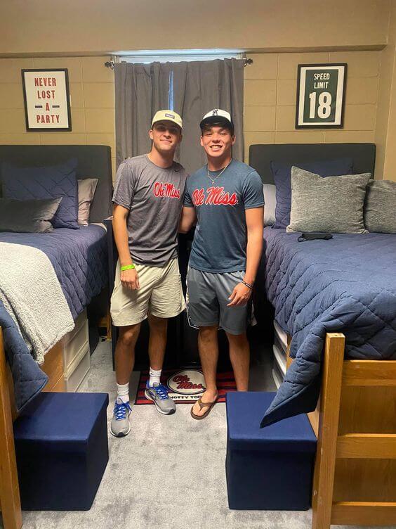 roommates standing in front of dorm beds with blue bedding