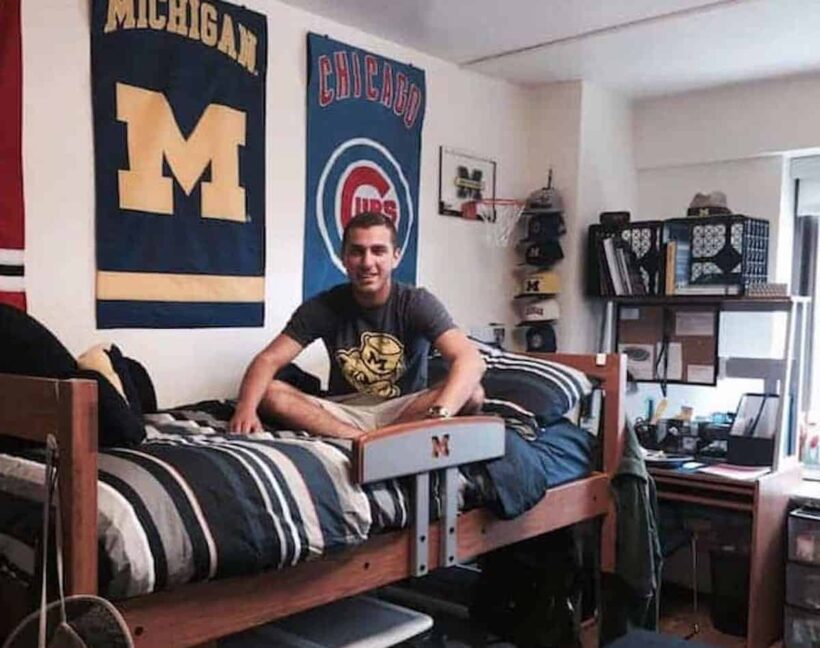 boy on dorm room bed with flags hanging behind him