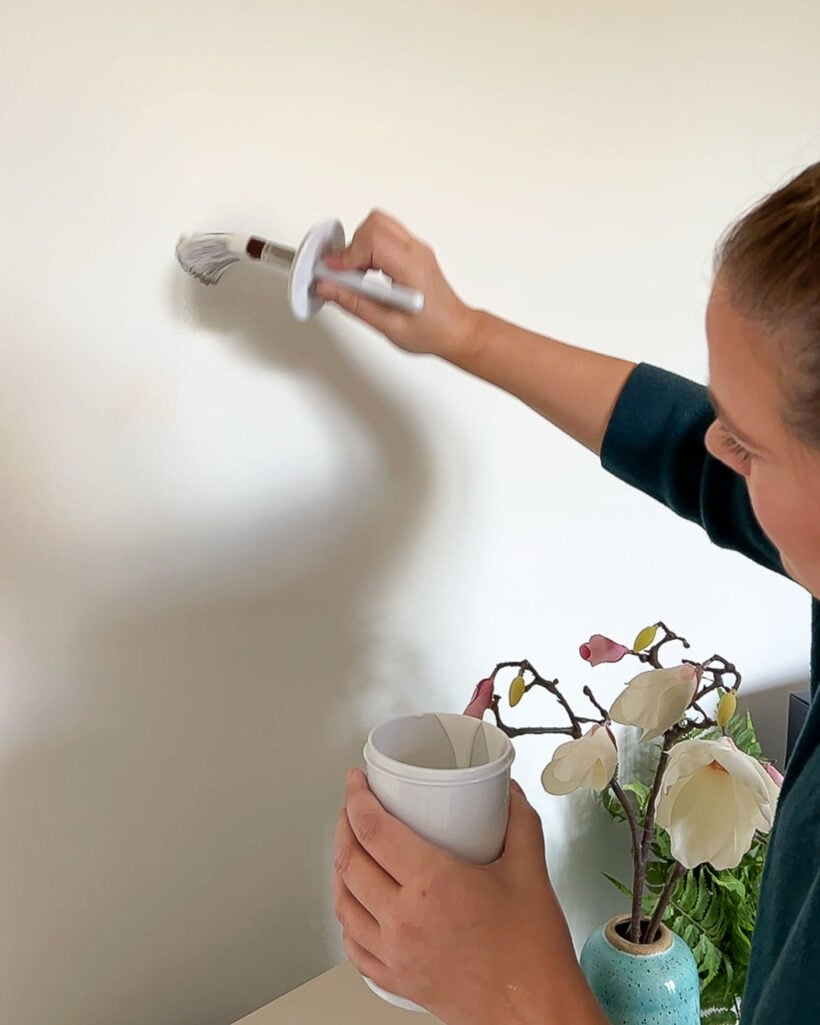 woman touching up paint on white wall