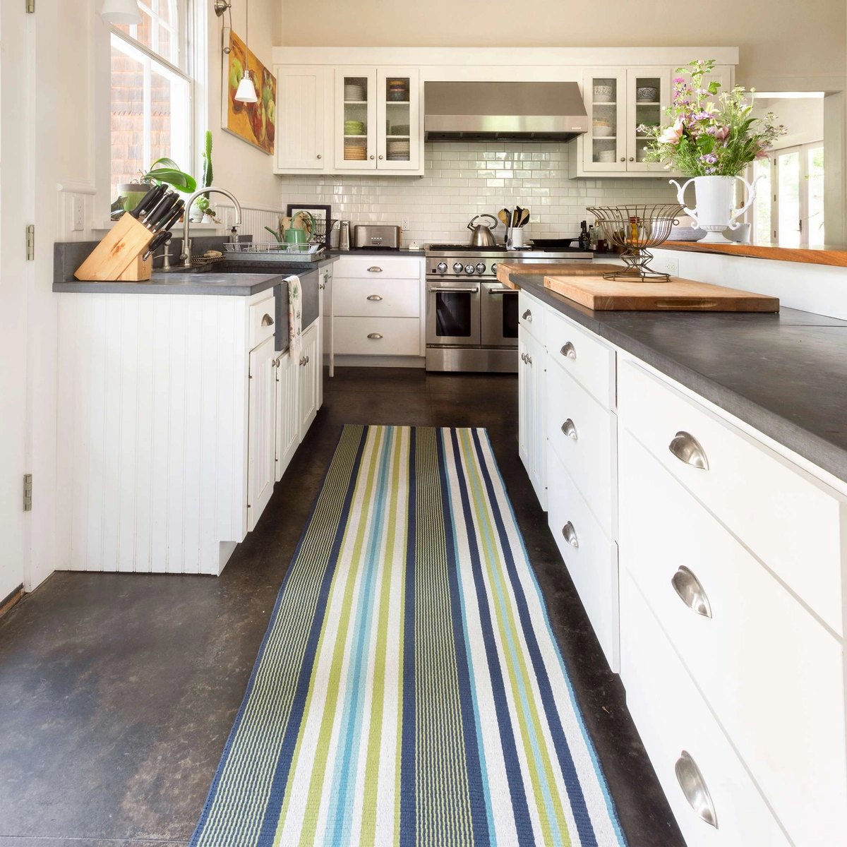 A striped indoor-outdoor rug used as kitchen runner in a long and open white kitchen. 