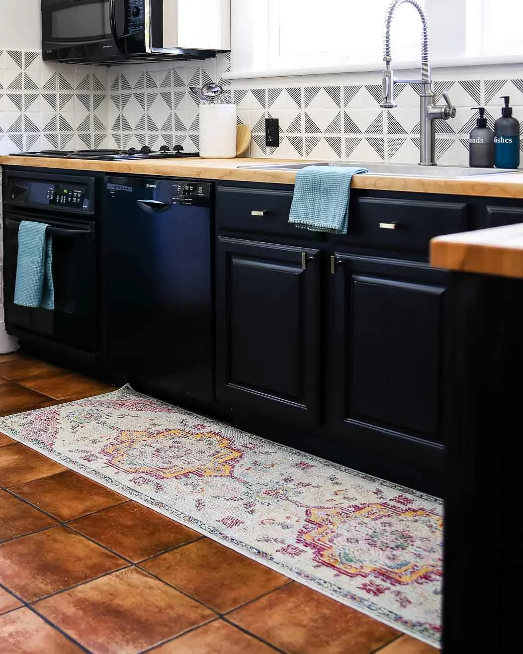 A length of muted-colors medallion kitchen rug runner in a black and white kitchen. 