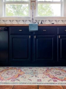 A light-colored medallion kitchen rug runner in front of dark sink and floor cabinets.