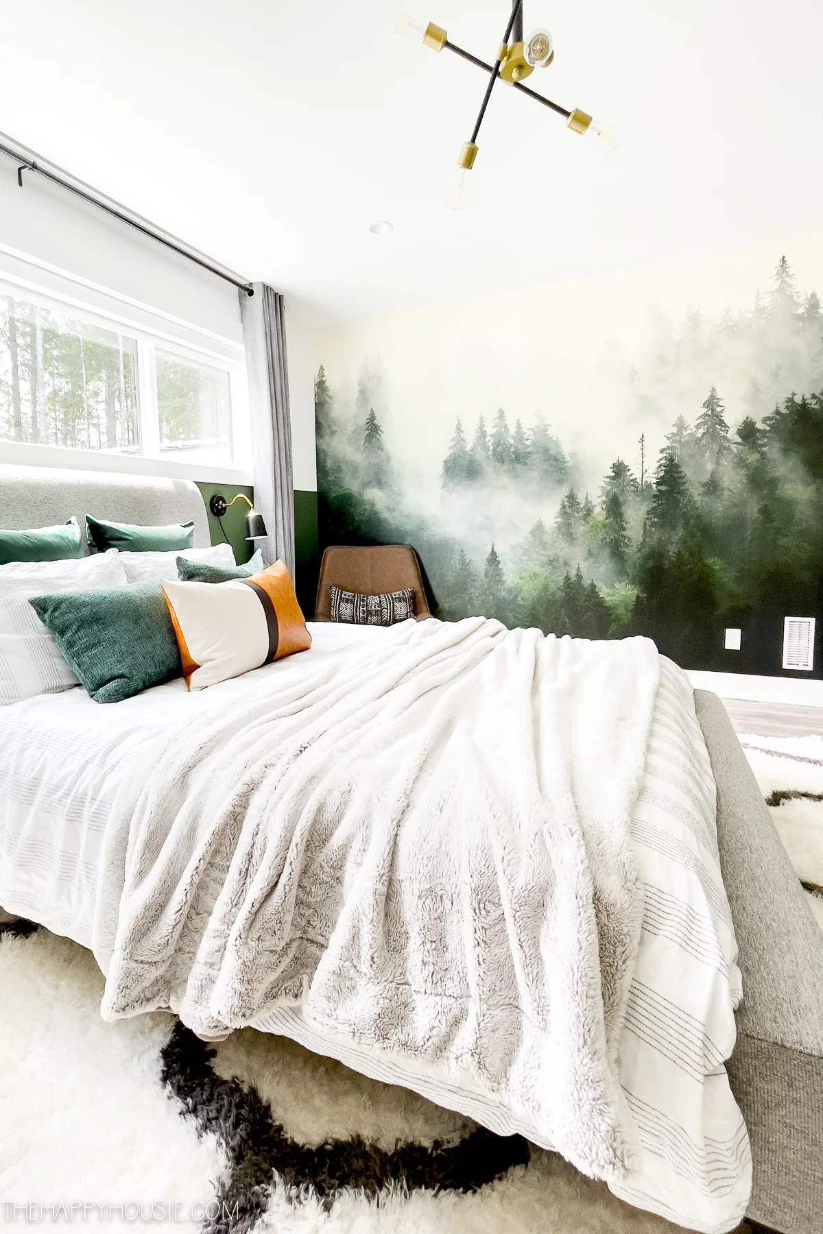 An evergreen forest wall mural next to a bed covered in white blankets in a teen boy's sunny bedroom