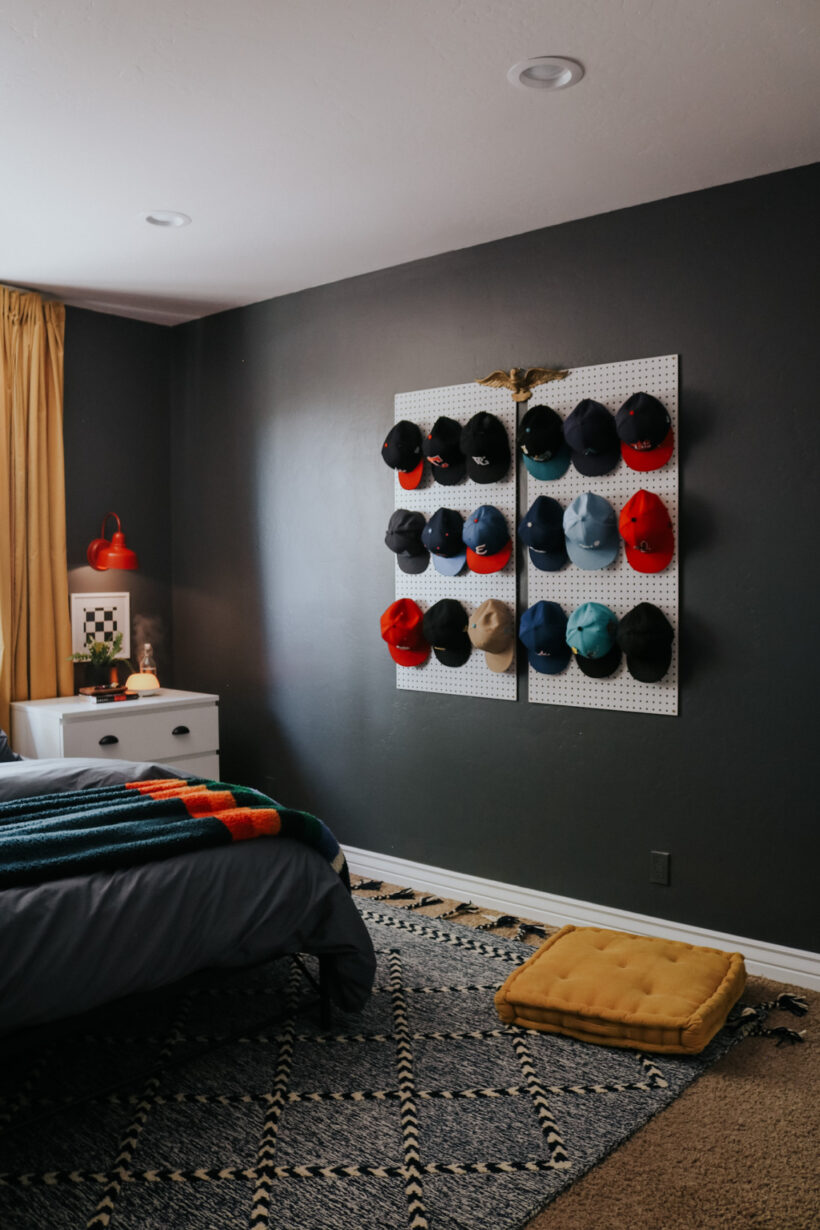 baseballs hats hanging on pegboard as art in teen boy's room