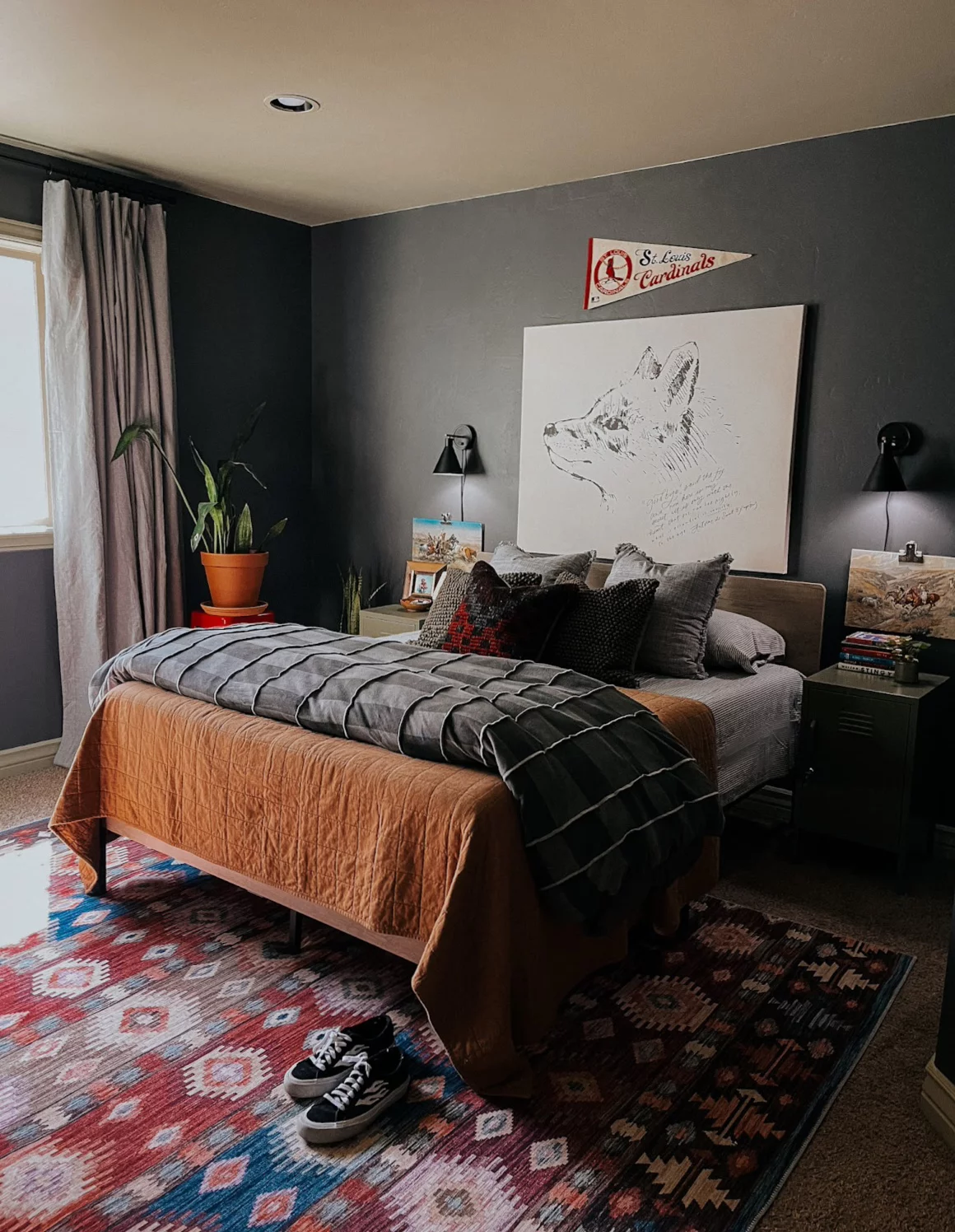 A dark grey boy's bedroom with layered, textured bedding, a potted plant, and large line drawing of a dog above the bed. 