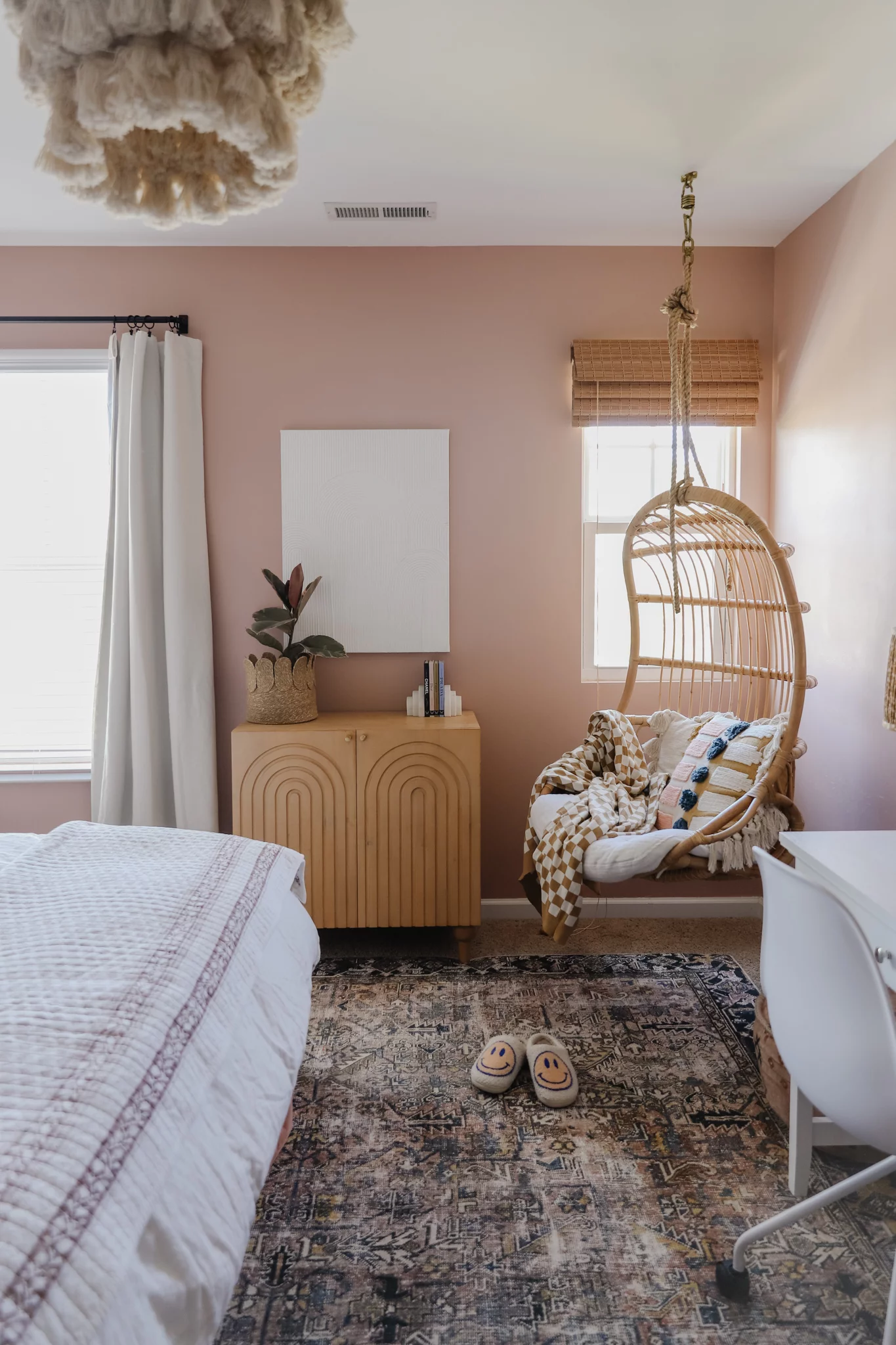 The corner of a teen girl's neutral-colored room with a hanging basket chair, cabinet wall unit and white bed and desk. 