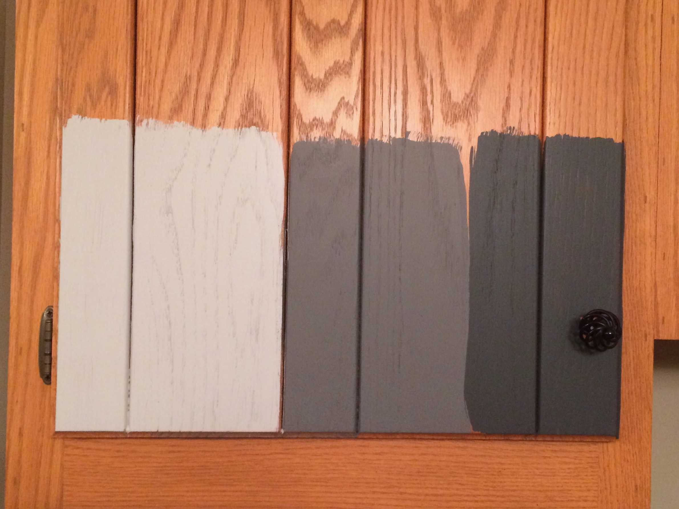 image of orangey oak kitchen cabinet door with three gray paint color samples from General Finishes Milk Paint painted on it