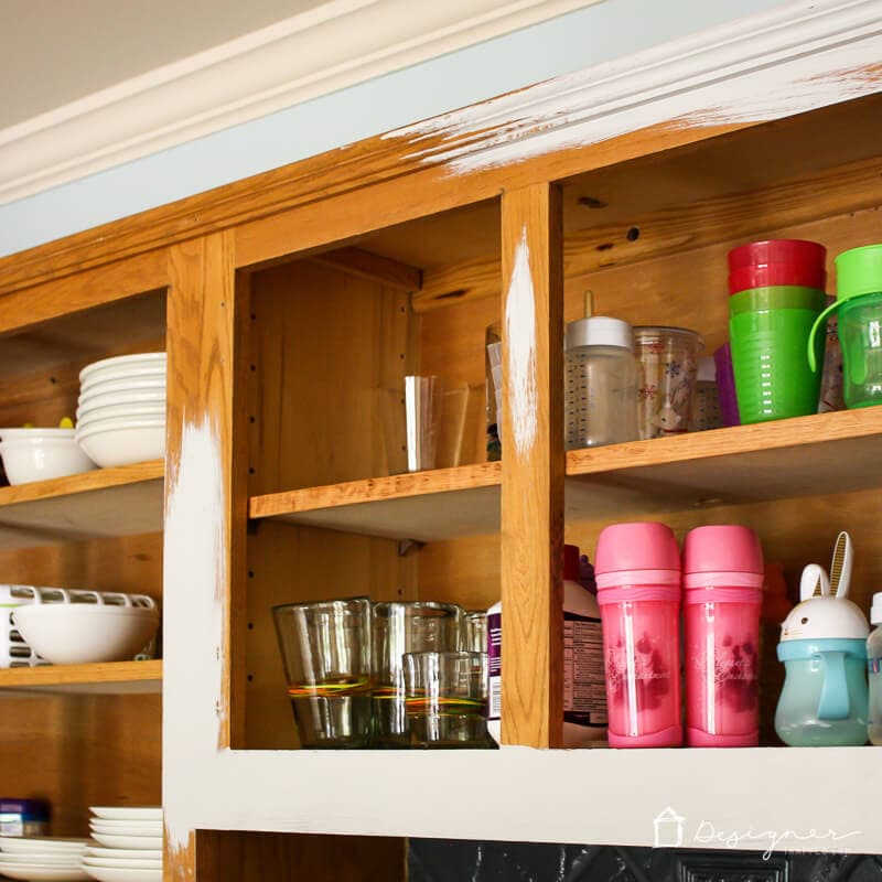photo of the frame of natural oak kitchen cabinet boxes being painted a light gray color with contents of kitchen cabinets still in place