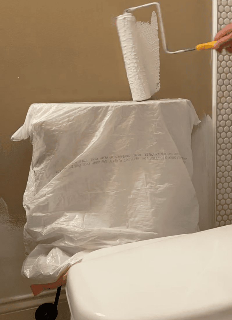 image of paint roller painting near toilet with the toilet tank protected by a plastic bag